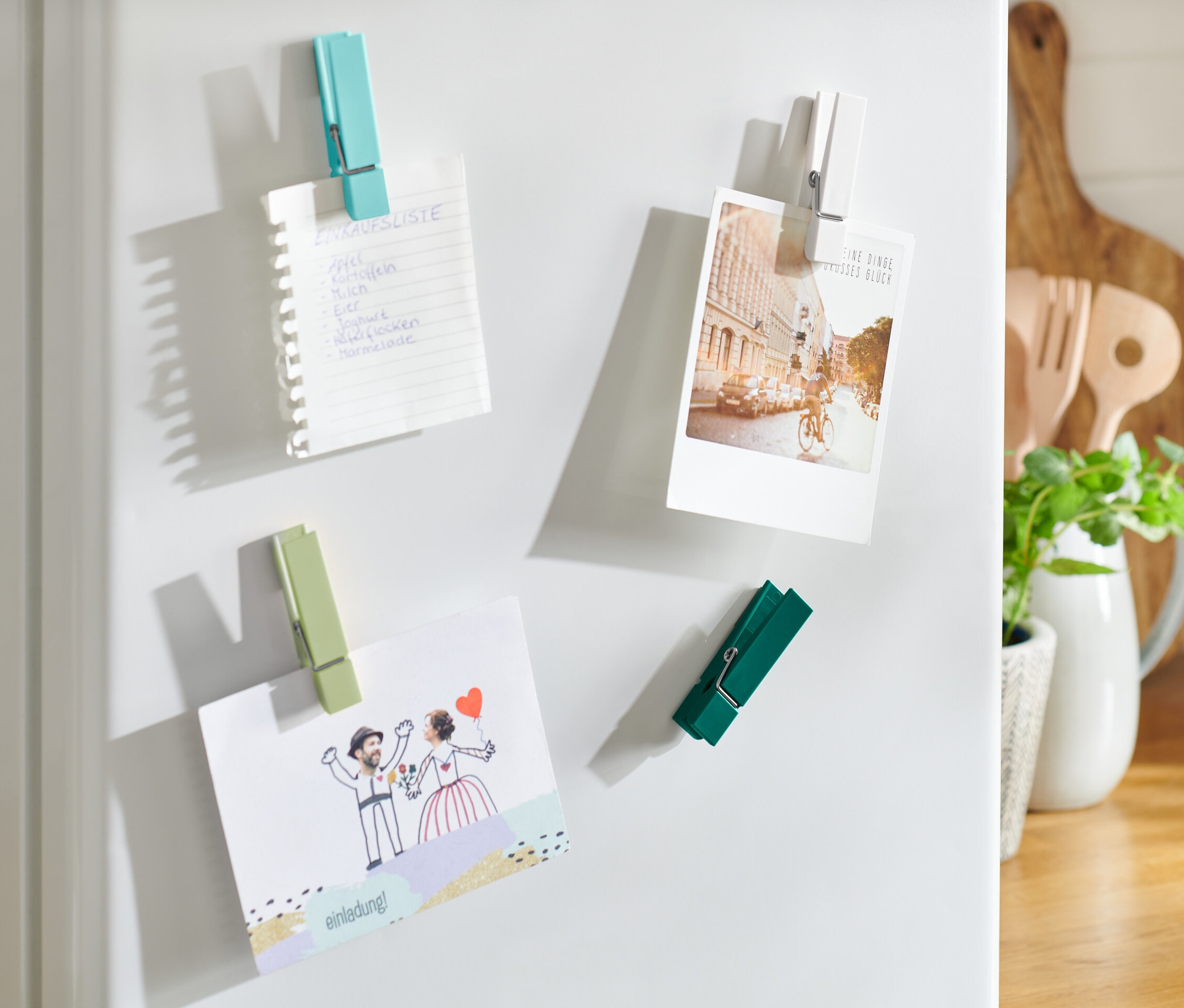 Štyri magnety na chladničku držia nákupný zoznam, pohľadnicu a pozvánku.