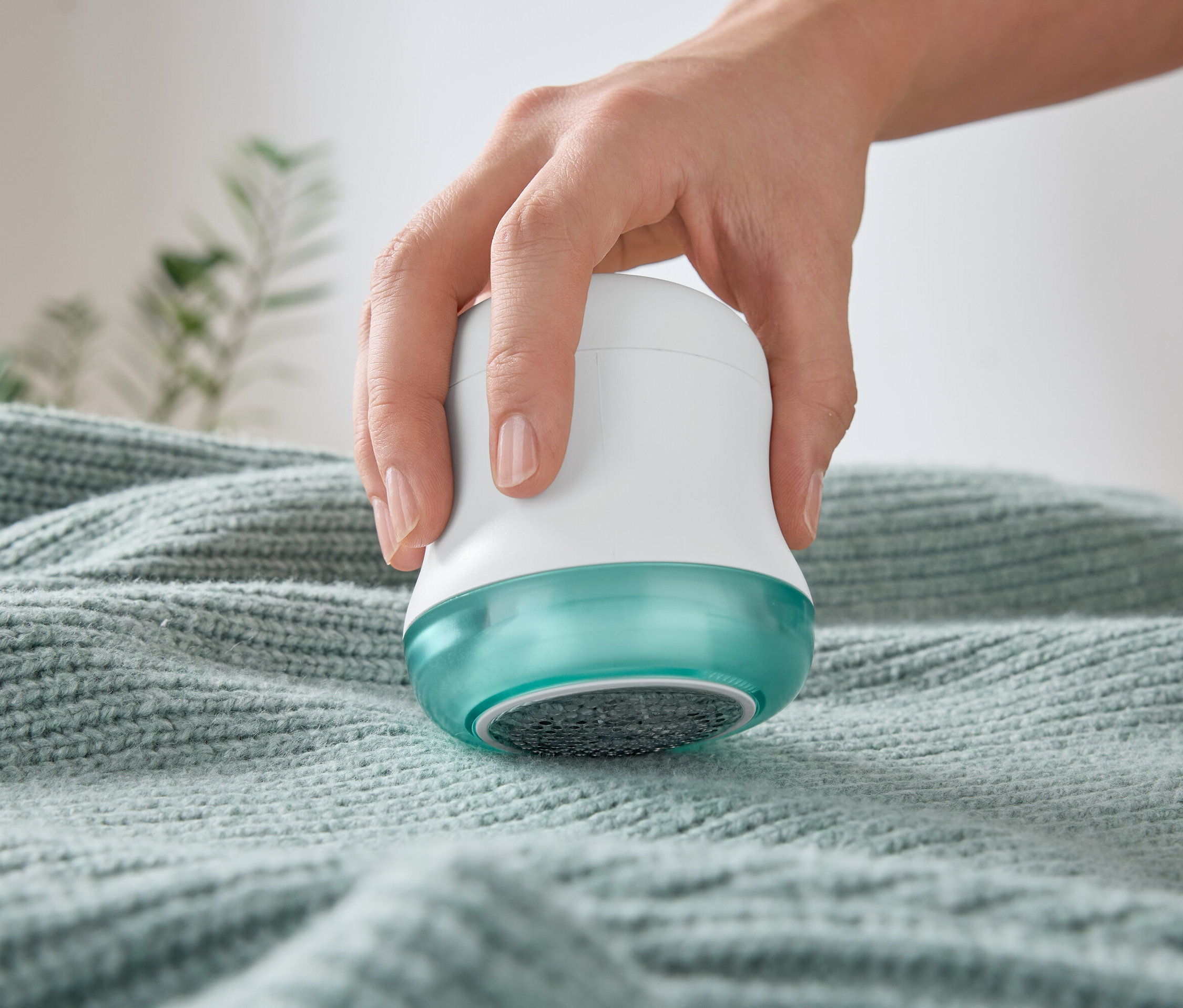 Ruka používa odstraňovač žmolkov na svetri.