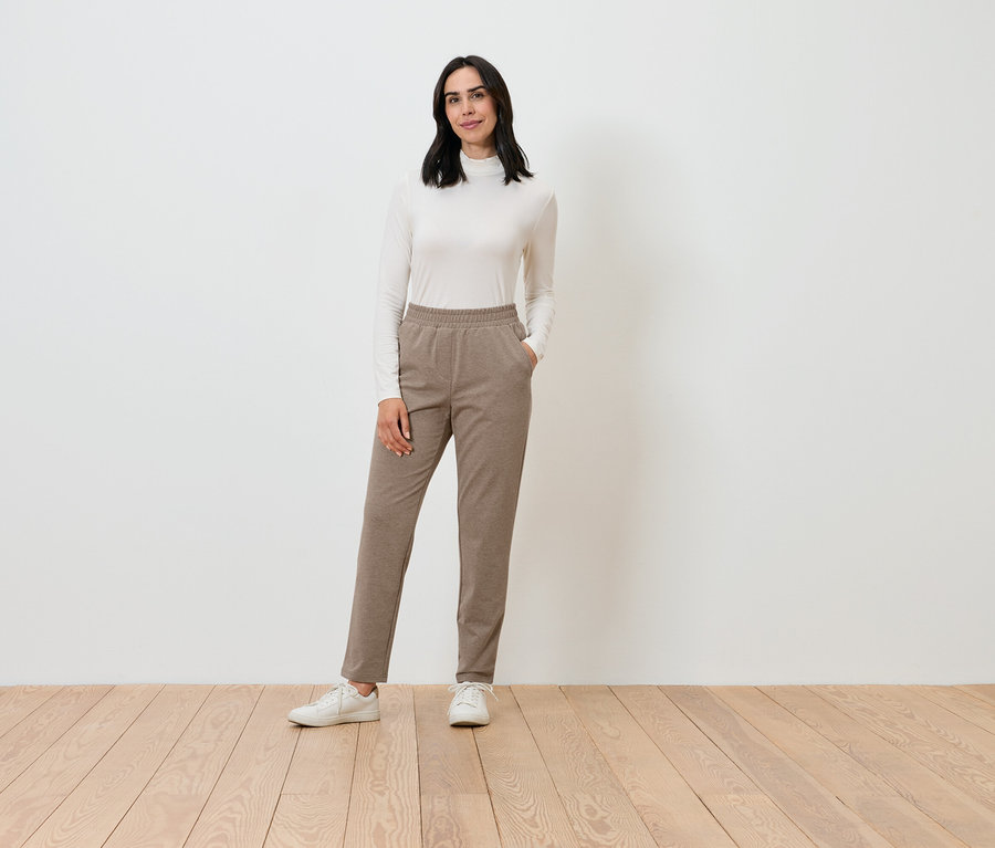 Žena pózuje v krémovom roláku a hnedých nohaviciach.