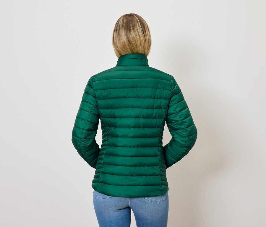 Pohľad zozadu na ženu s blond vlasmi v zelenej prešívanej bunde a modrých džínsoch.