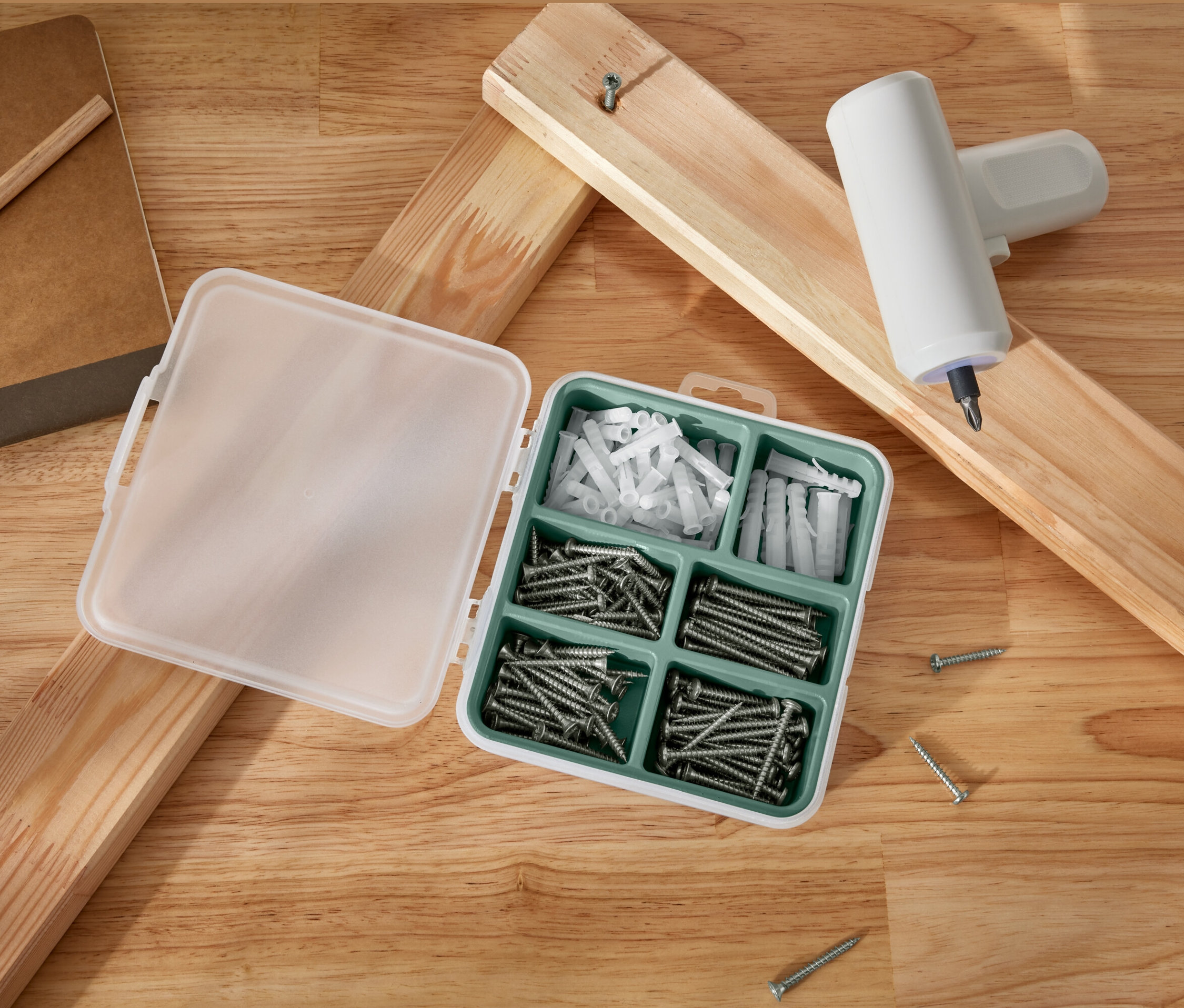 Otvorená sada skrutiek a hmoždiniek leží vedľa drevených dosiek a akumulátorového skrutkovača.