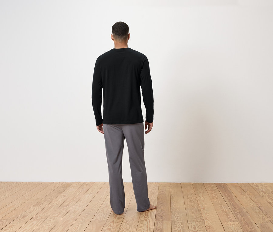 Muž chrbtom k fotoaparátu má na sebe čierne tričko s dlhým rukávom a sivé nohavice.