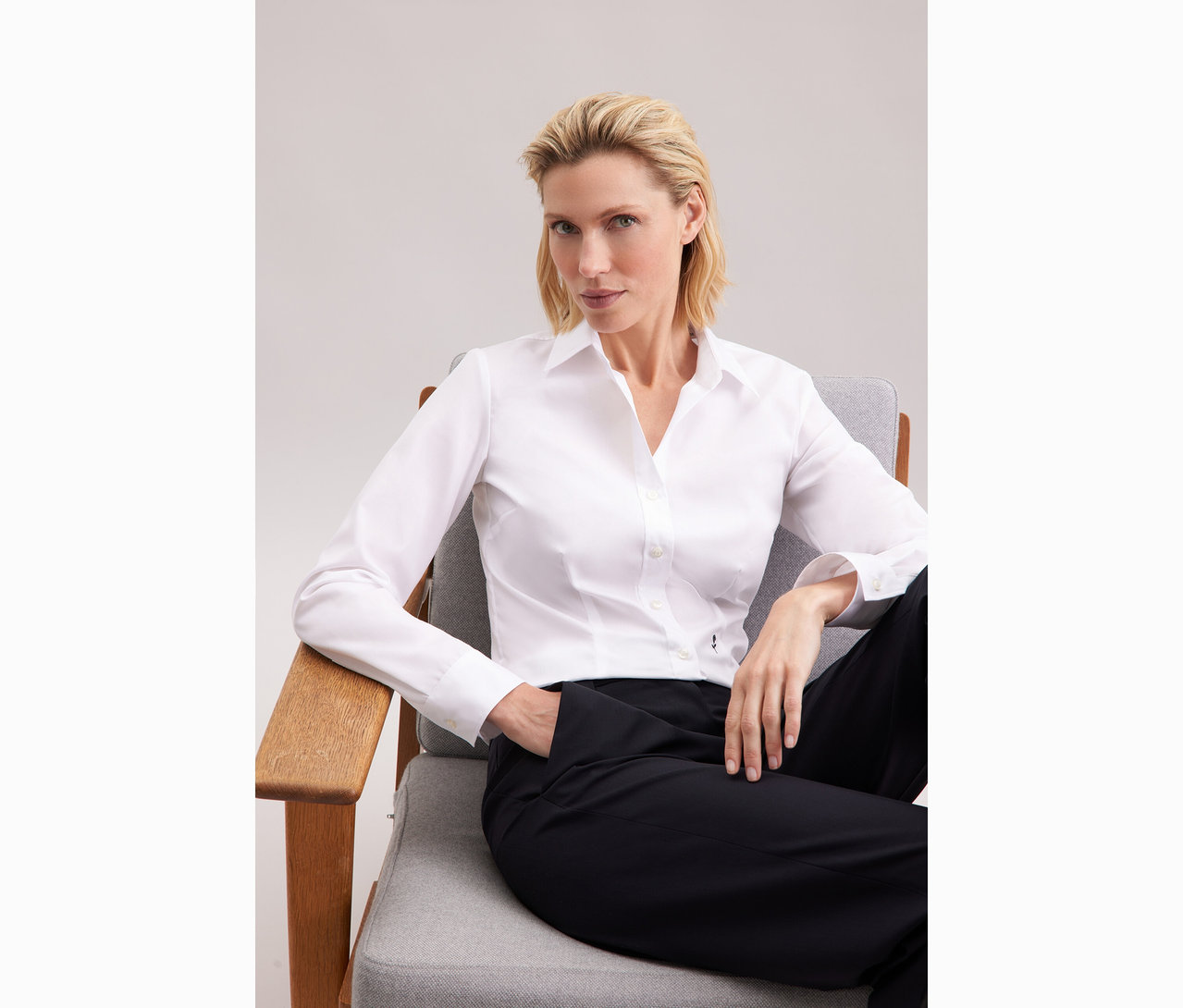 Žena sedí na stoličke a má na sebe bielu blúzku Seidensticker Slim Fit non iron.