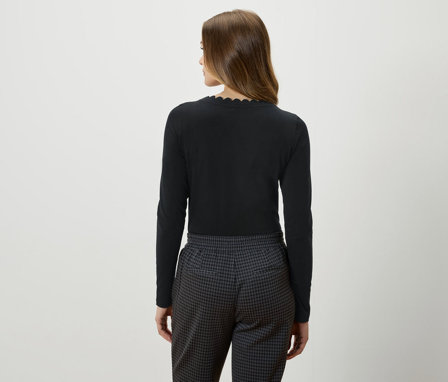 Pohľad zozadu na ženu s hnedými vlasmi v čiernom tope s dlhým rukávom a sivo-čiernych nohaviciach.