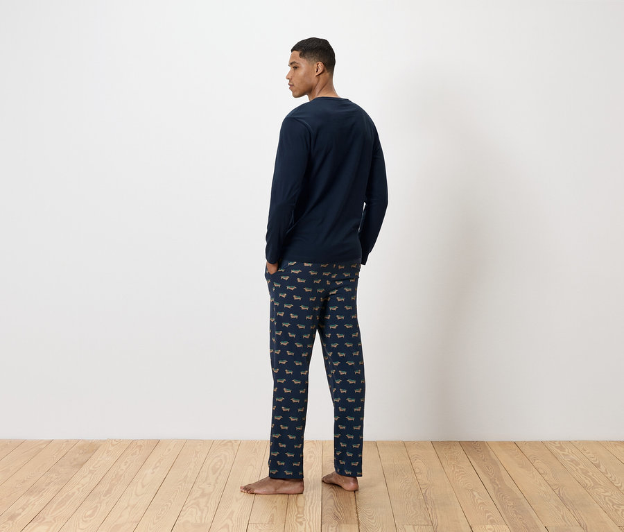 Muž chrbtom k fotoaparátu má na sebe tmavomodré pyžamo s potlačou jazvečíkov.