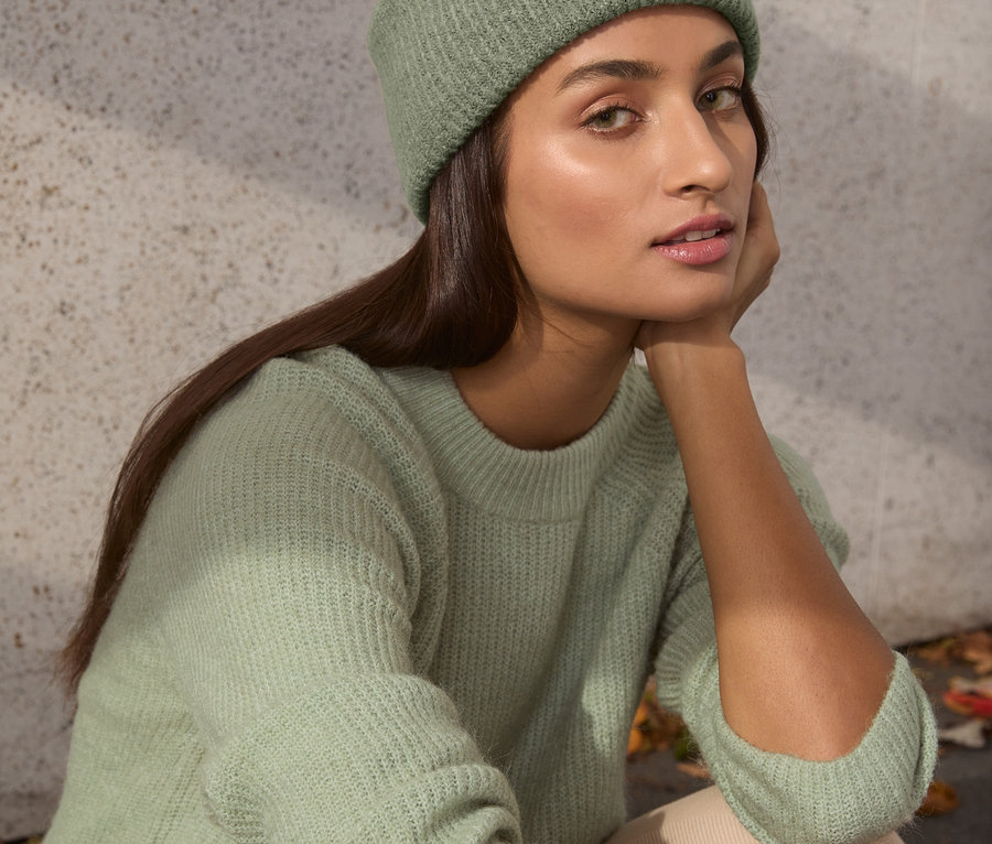 Žena sedí a má na sebe šalviový pulóver z hrubej pleteniny a zodpovedajúcu čiapku.