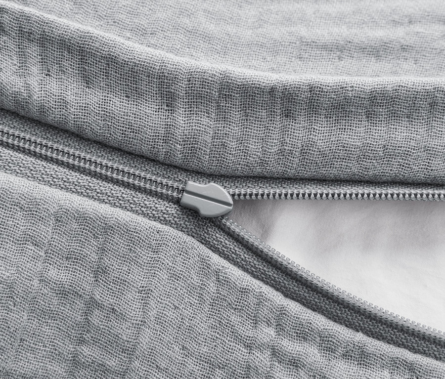 Detail šedého obliečky na paplón so zipsom, ktorý je čiastočne rozopnutý a odhaľuje bielu výplň.