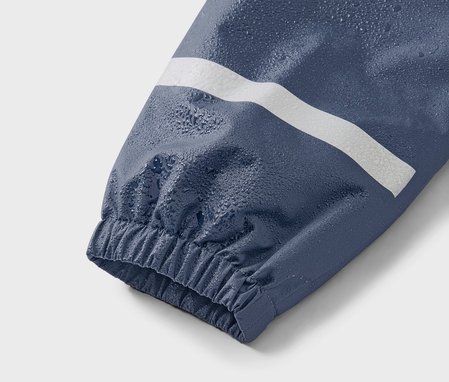 Detailný záber na modrý rukáv bundy s bielym pruhom a kvapkami vody.