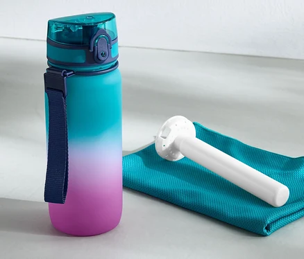 Fľaša na pitie s chladiacim akumulátorom stojí vedľa uteráka a kettlebell činky.