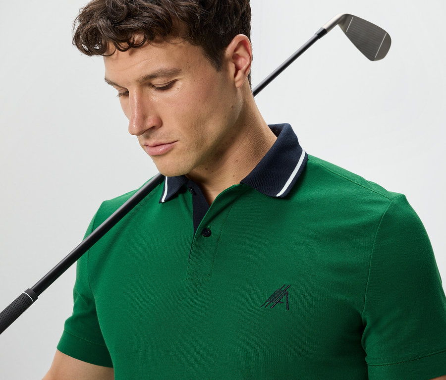 Muž s golfovou palicou cez plece má na sebe zelenú polokošeľu.