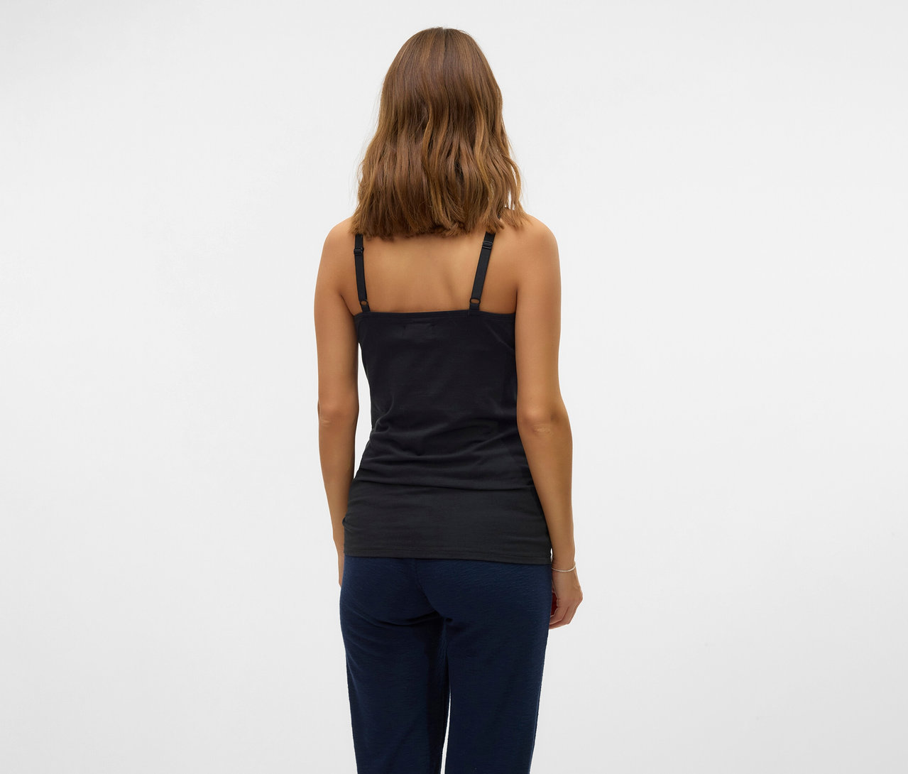 Žena zozadu v čiernom tielku s tenkými ramienkami MAMALICIOUS v 2-balení »MLKERRIE« a v modrých nohaviciach na bielom pozadí.