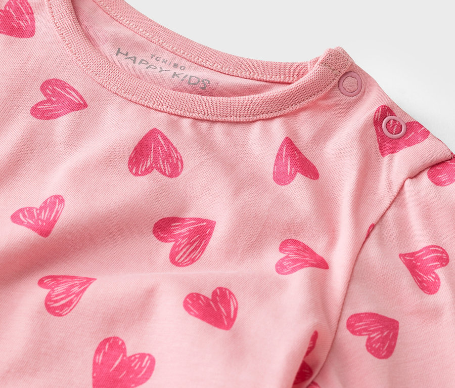 Detail ružového trička s dlhým rukávom so vzorom srdca a patentkami na golieri.