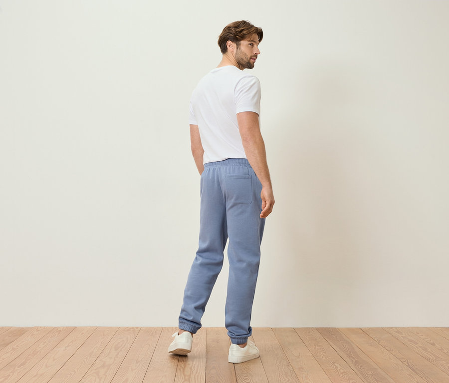 Muž v svetlomodrých teplákoch a bielom tričku, pohľad zozadu.