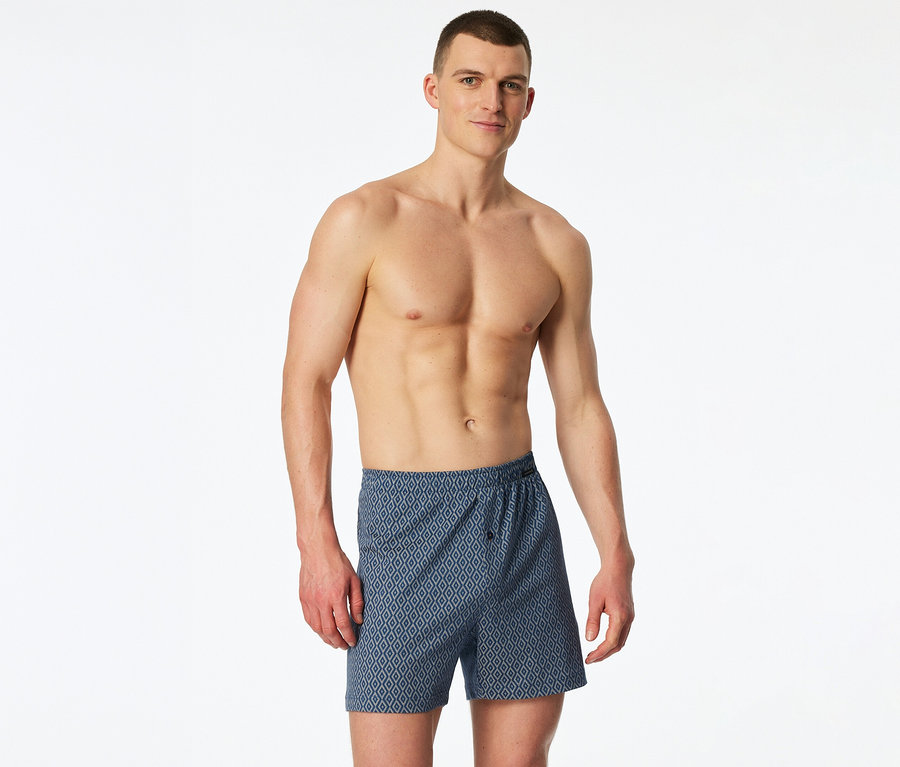 Muž bez trička má na sebe modré džersejové boxerky SCHIESSER so vzorom kosoštvorcov.