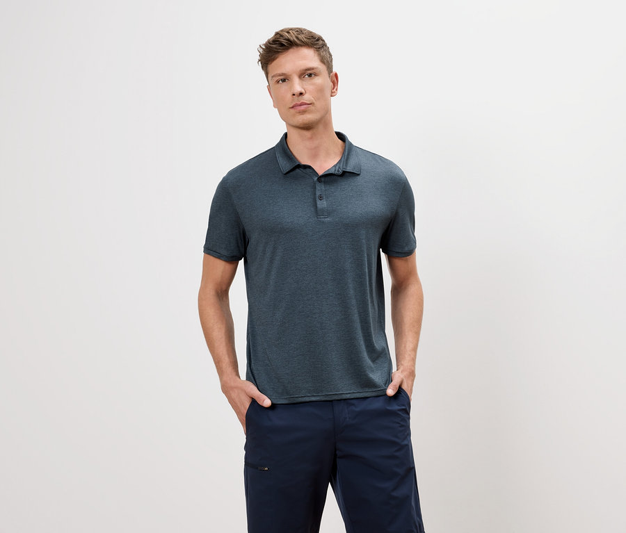 Muž v modrom polo tričku a modrých šortkách stojí na bielom pozadí.