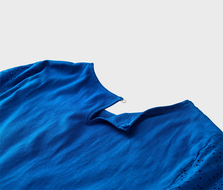 Detailný záber na kobaltovo modrý top s rukávmi s dierkovanou výšivkou a detailmi gombíkov.