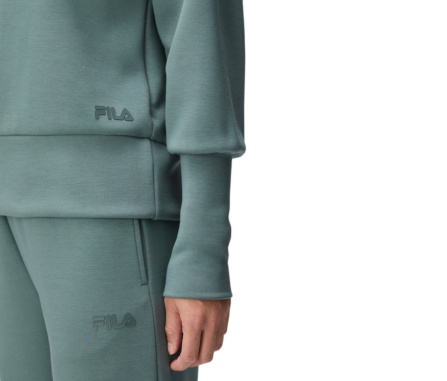 Detailný záber osoby v tyrkysovej teplákovej súprave Fila, s logom Fila na vrchnom aj spodnom diele.