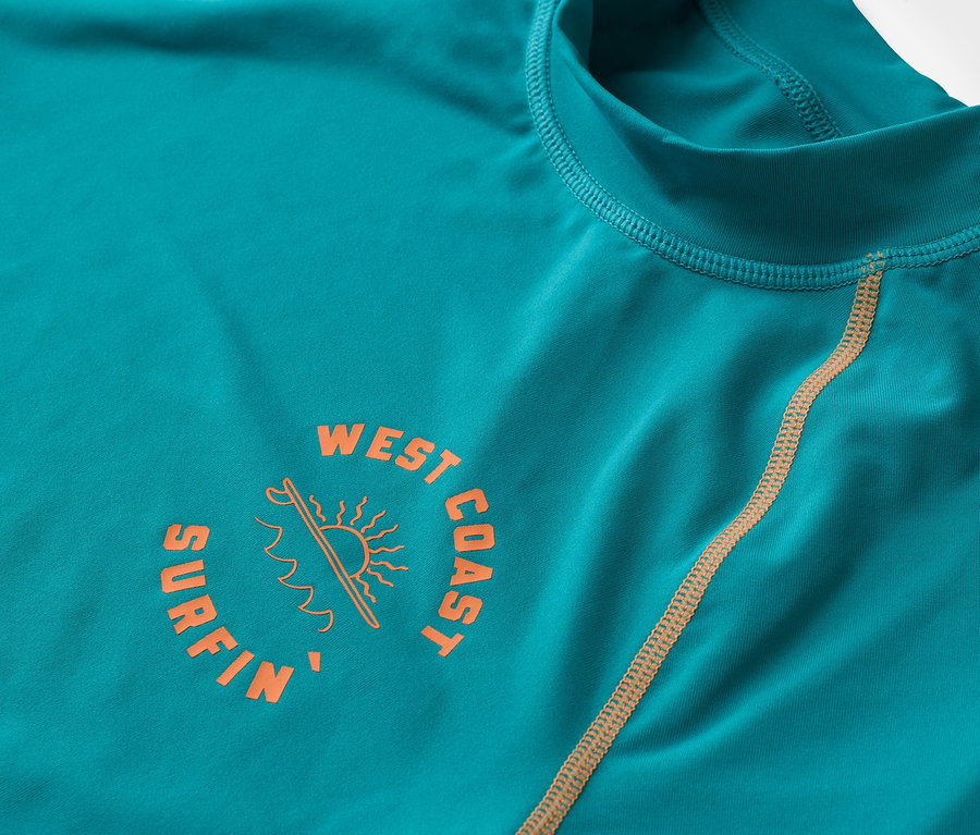 Detailný záber na tyrkysové tričko s dlhým rukávom s oranžovým logom "West Coast Surfin".