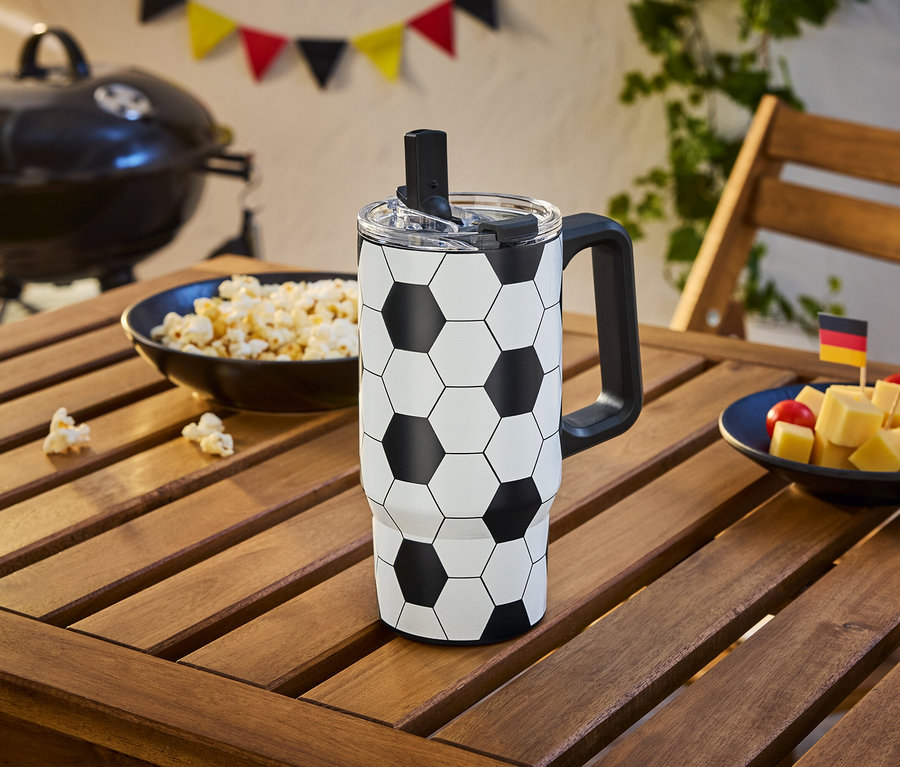 Na drevenom stole stojí futbalový pohár vedľa misky popcornu a kociek syra s nemeckou a španielskou vlajkou.