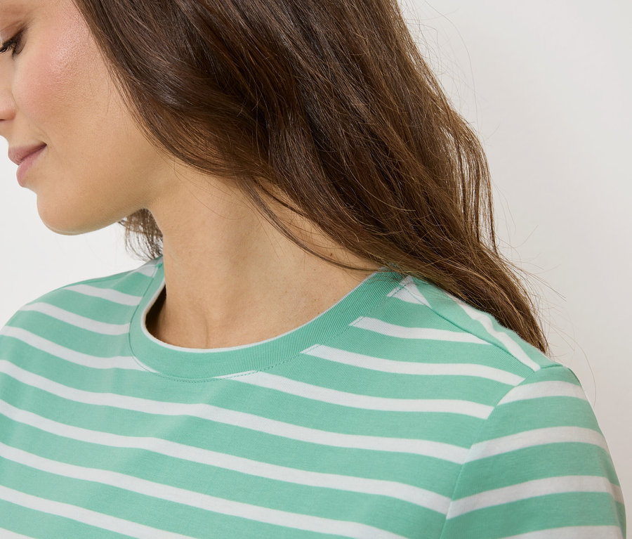 Detailný záber ženy s hnedými vlasmi v zeleno-bielom pruhovanom tričku.