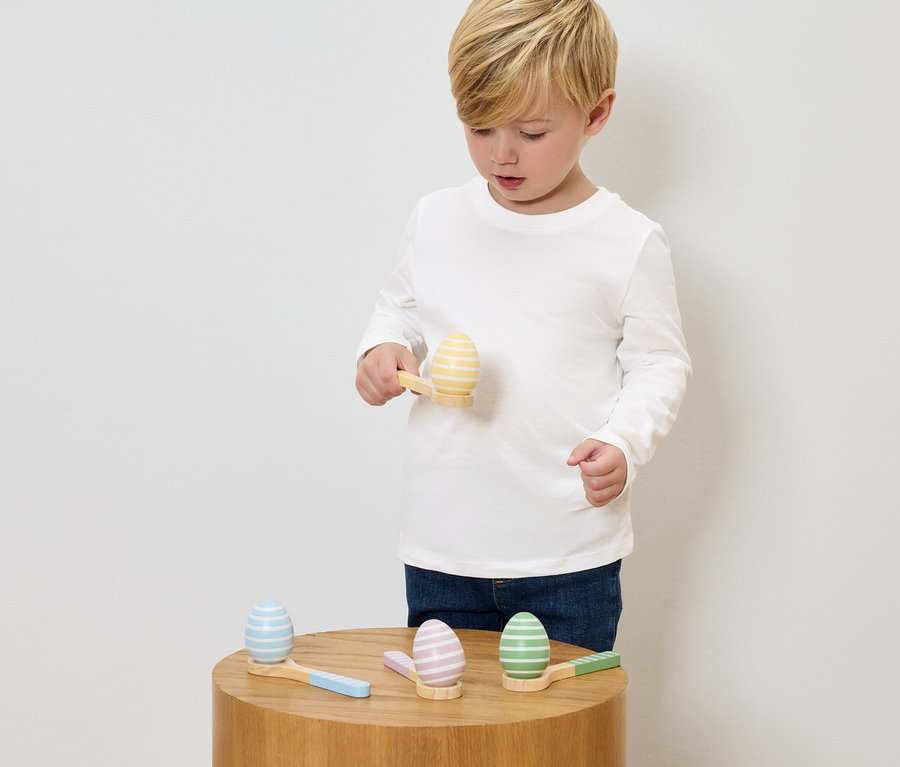 Chlapec sa hrá s maľovanými drevenými vajíčkami a malými kladivkami na drevenom stole.