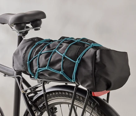 Čierna taška na bicykel je pripevnená k čiernemu nosiču bicykla pomocou modrej batožinovej siete.