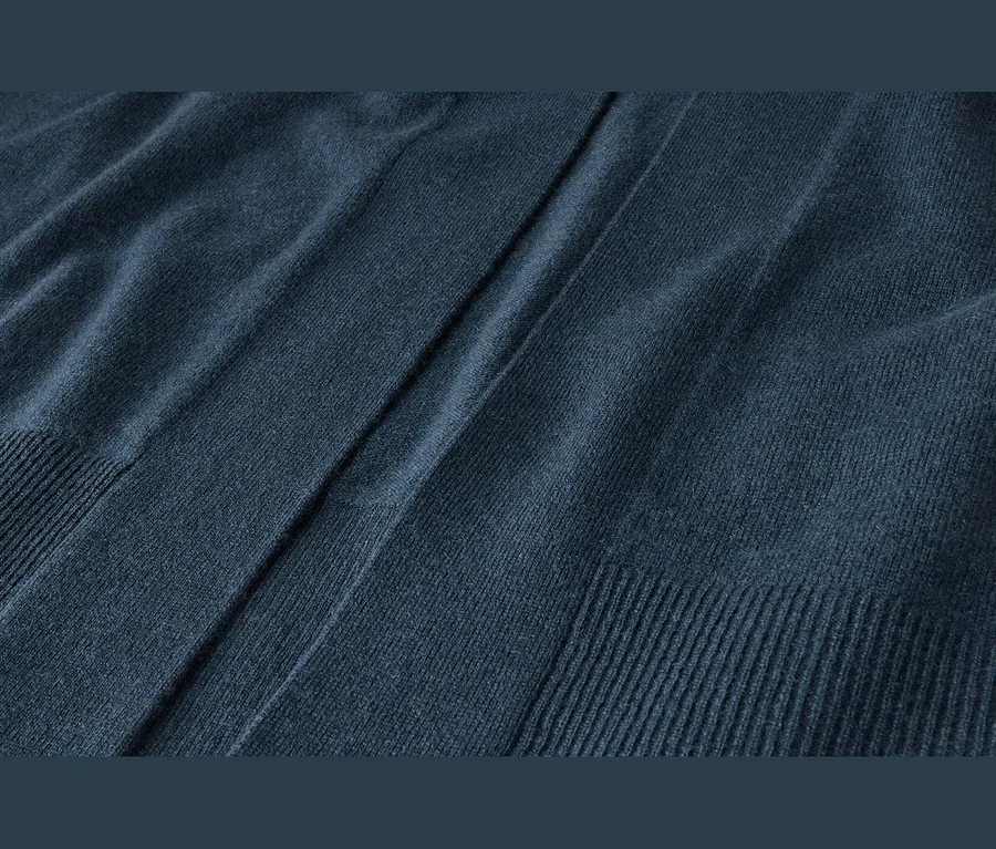 Detail tmavomodrej pletenej látky s mäkkou textúrou, záhybmi a rebrovanými okrajmi.