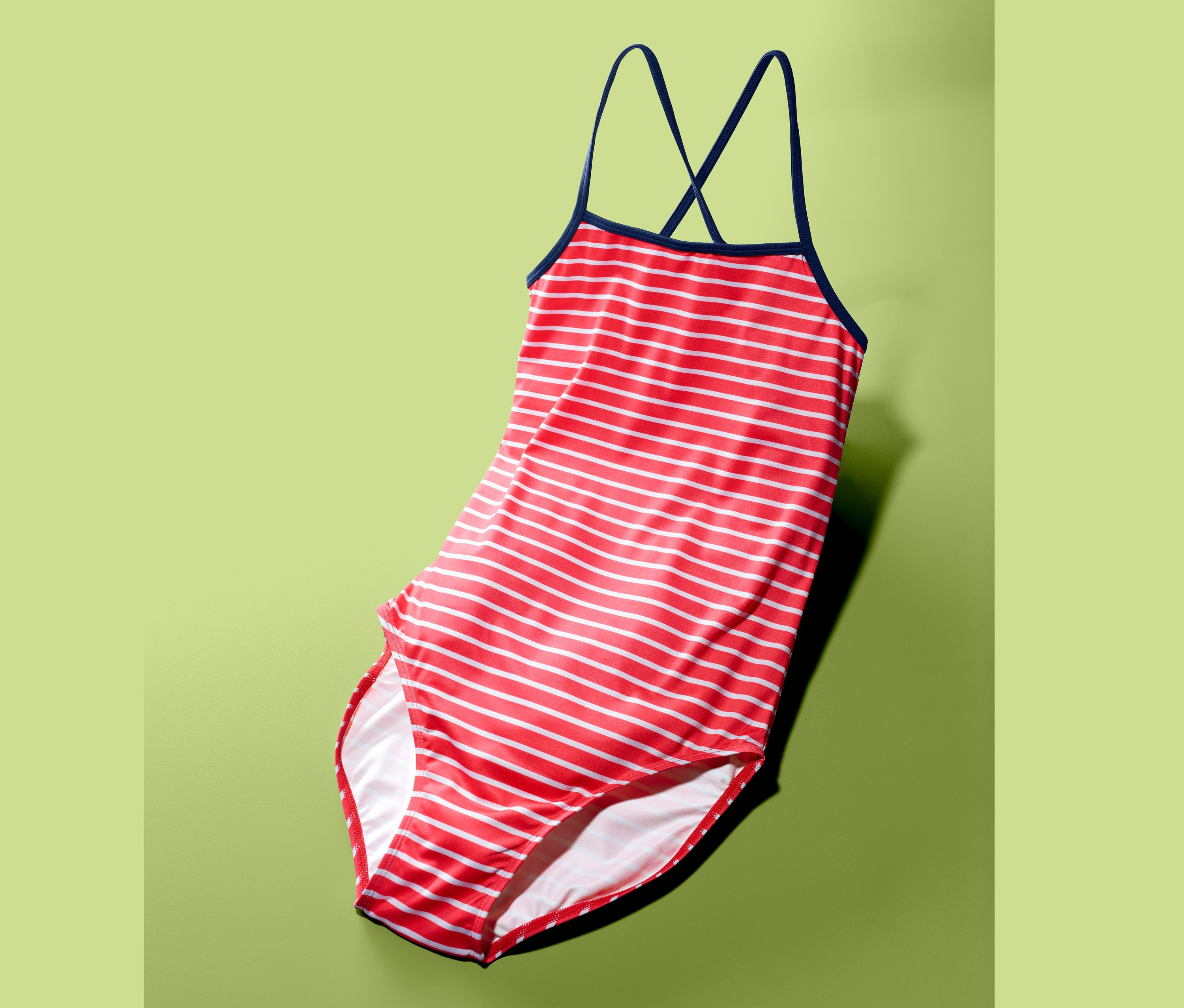 Červeno-biely pruhovaný jednodielne plavky s tmavomodrými ramienkami na zelenom pozadí.