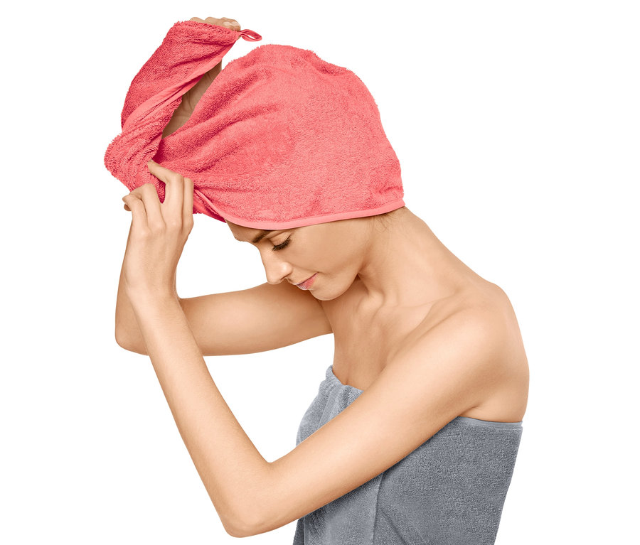 Žena si upravuje ružový uterákový turban na hlave, telo má omotané sivým uterákom.