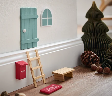 Súprava miniatúrneho nábytku na stene s miniatúrnymi vianočnými stromčekmi a dekoráciami.