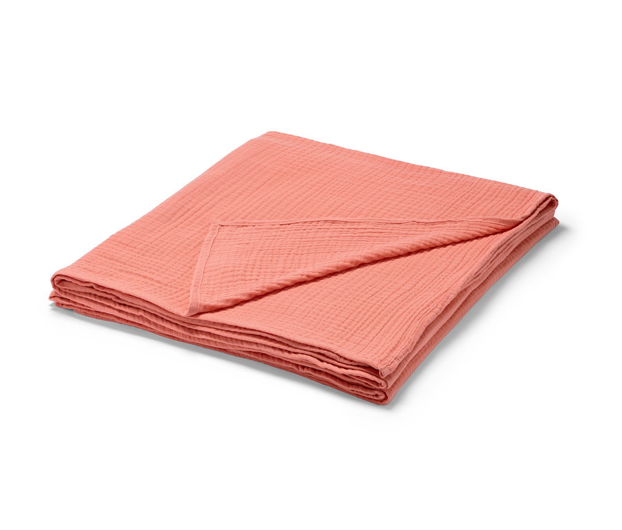 Zložený broskyňový prehoz na posteľ z mušelínu.