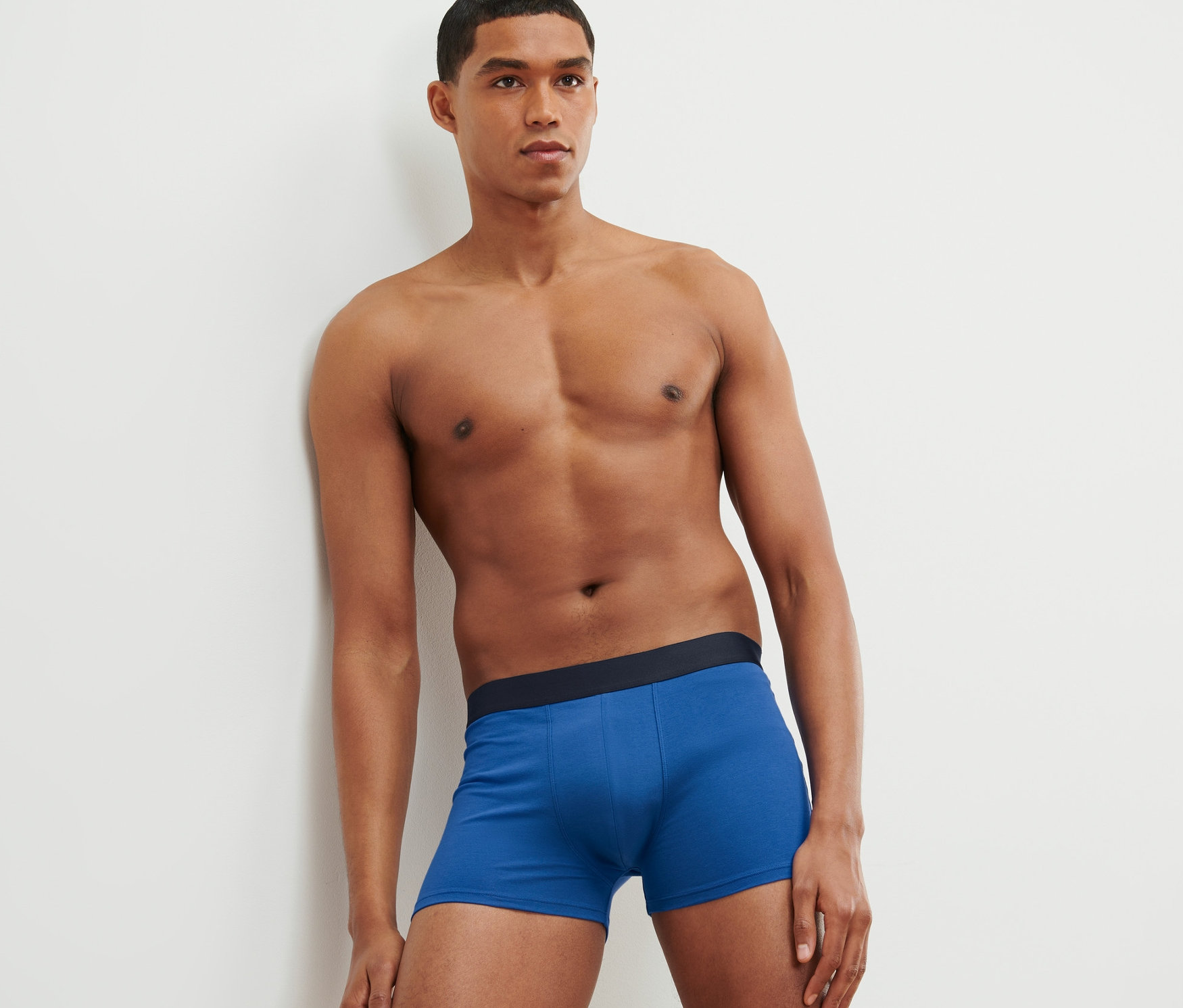 Muž opretý o stenu má na sebe modré boxerky, celoplošná potlač a sivé, 4 ks.