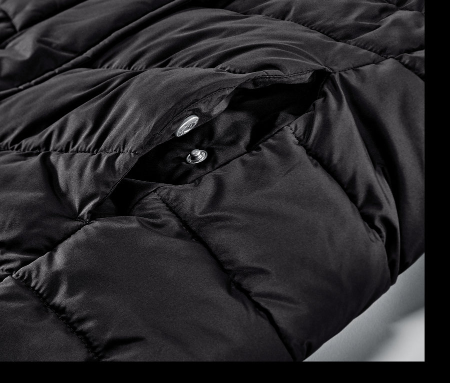 Detail čierneho prešívaného kabáta s kapucňou a patentkami.