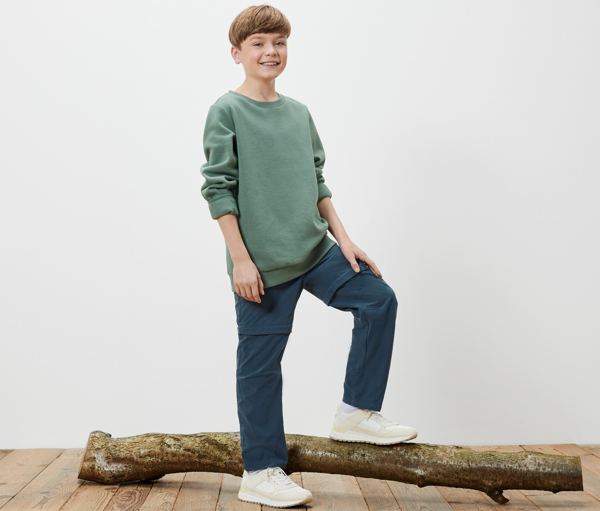 Chlapec stojí na kmeni stromu a má na sebe detské funkčné nohavice.