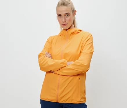 Žena pózuje so skríženými rukami v oranžovej skladacej funkčnej bunda.