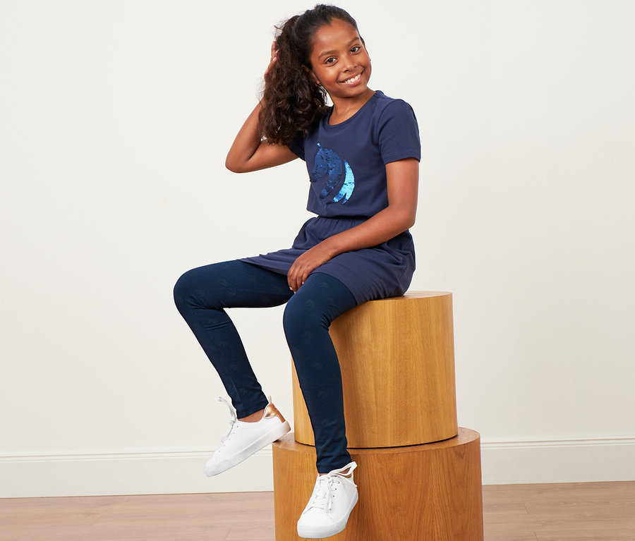 Dievča sedí na drevenom bloku a má na sebe modré šaty a detské legínsy, 2 ks.