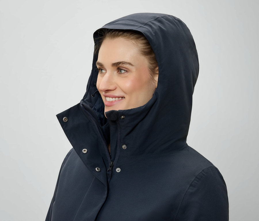 Žena s kapucňou a tmavomodrou bundou sa pozerá doprava.