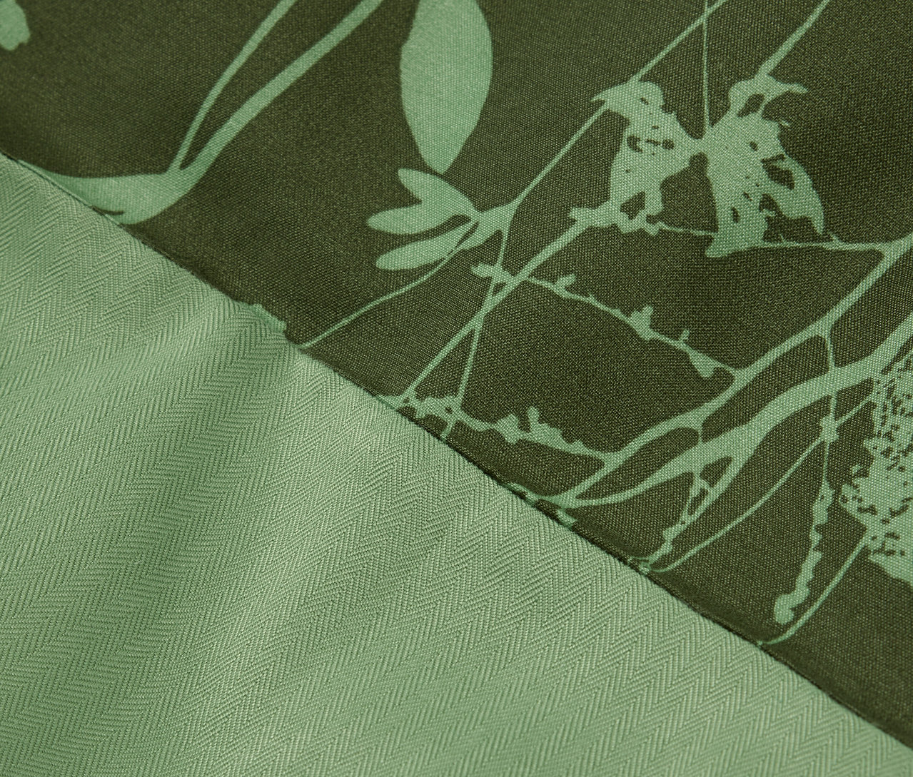 Detail zelenej látky s kvetinovou potlačou a textúrou rybej kosti.