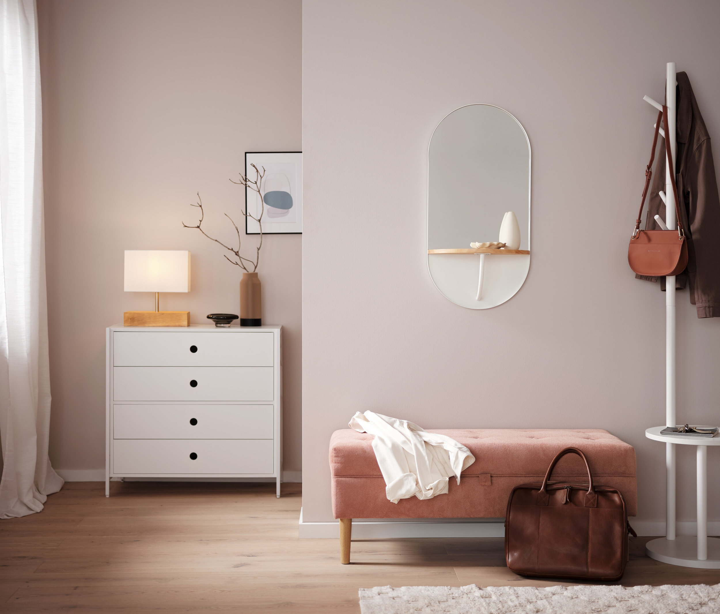 Spálňa s bielou komodou, zrkadlom a ružovou lavicou.