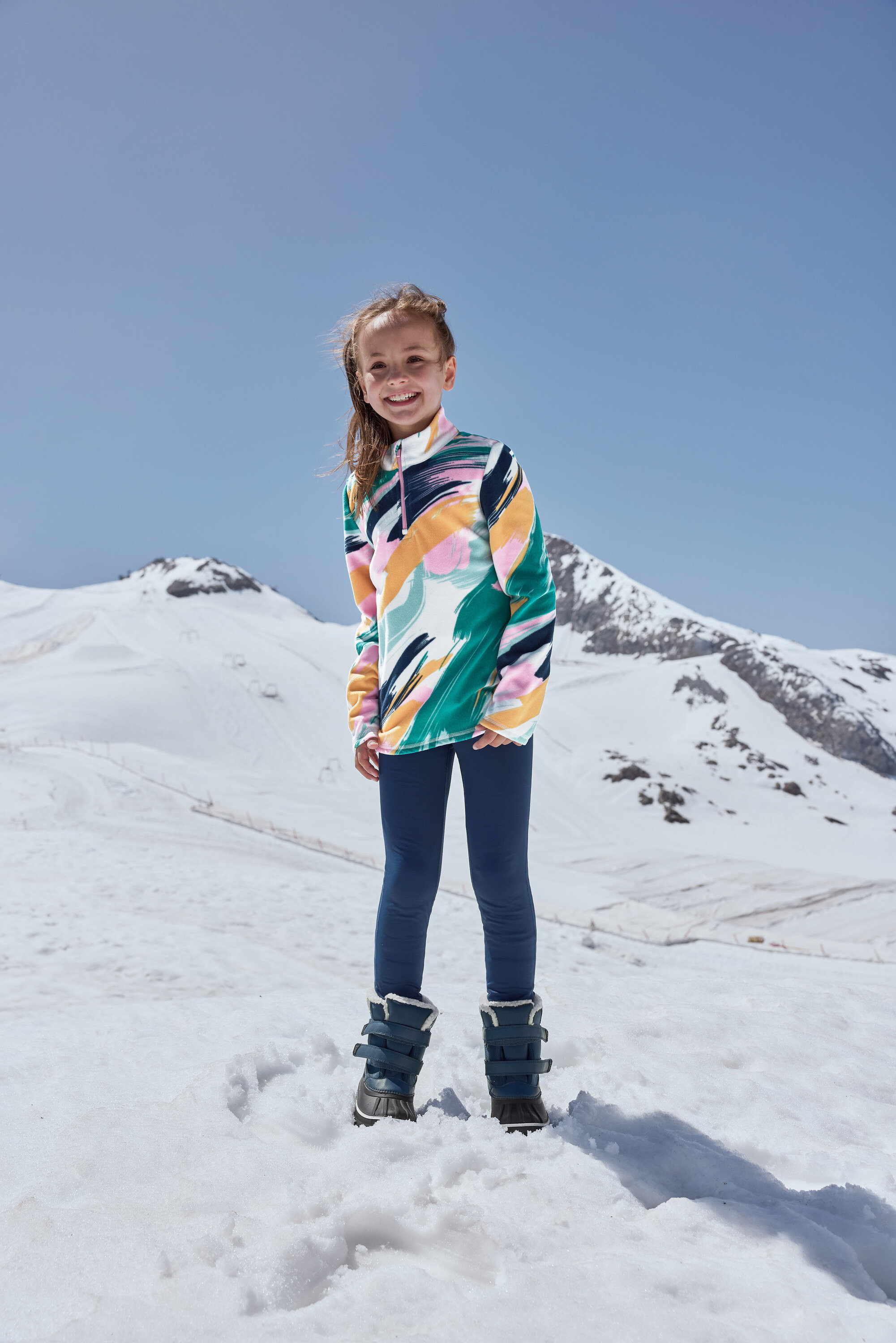 Usmievavé dievča stojí v snehu a má na sebe modré detské topánky do každého počasia.