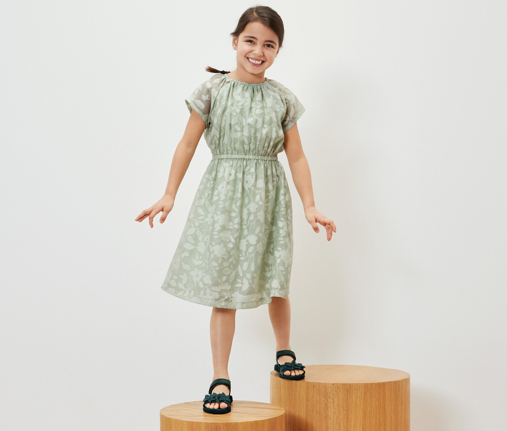 Usmievavé dievča stojí na drevených stupňoch a má na sebe detské šaty.