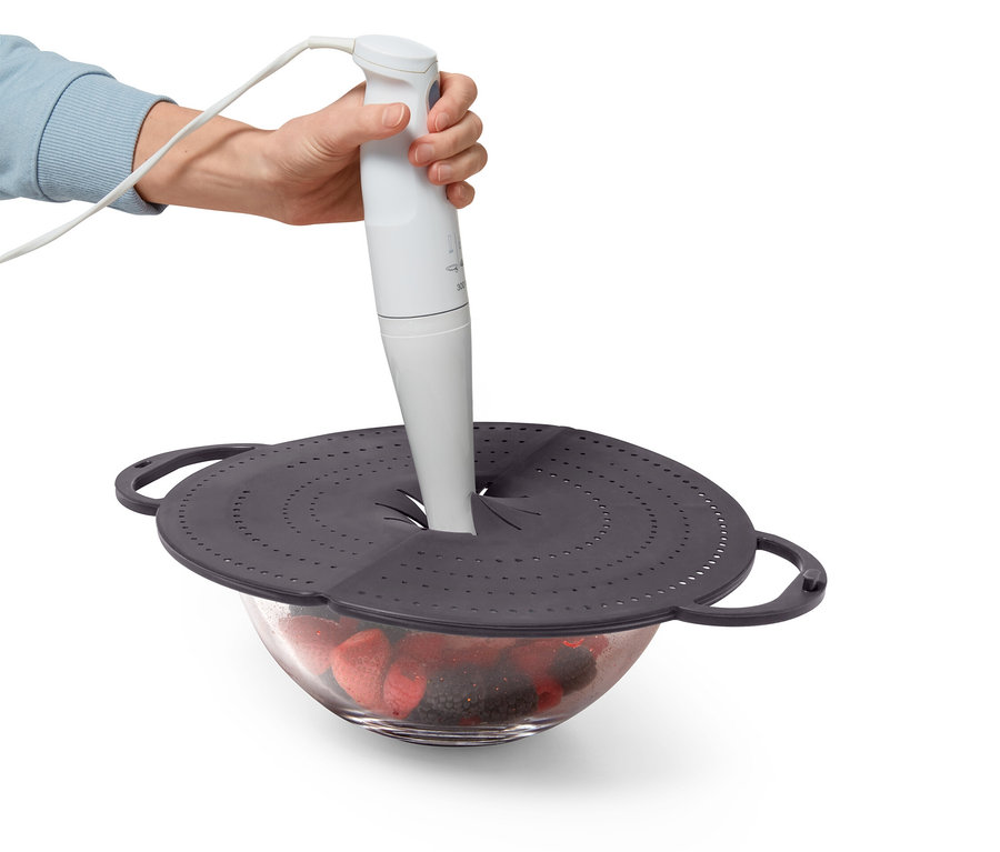 Ruka drží biely tyčový mixér nad misou s ovocím, ktorá je zakrytá sivým vekom s otvormi.