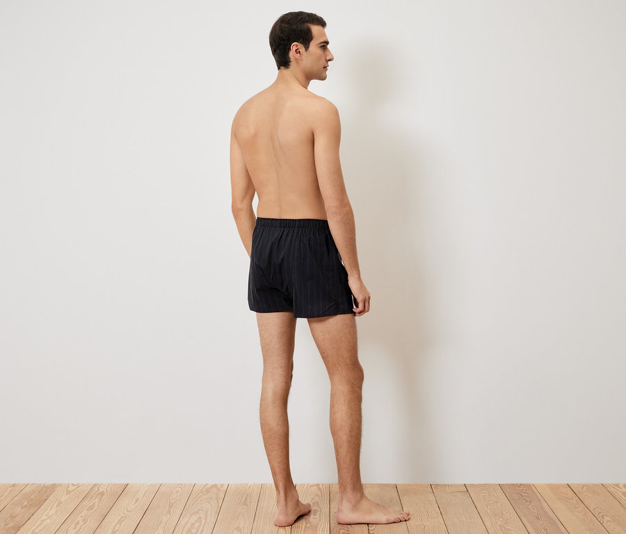 Muž zozadu, má na sebe čierne trenírky na drevenej podlahe.