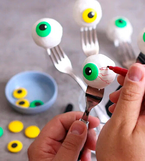 Ruka kreslí červenou fixkou červené žilky na bielu očnú buľvu s dúhovkou na vidličke.