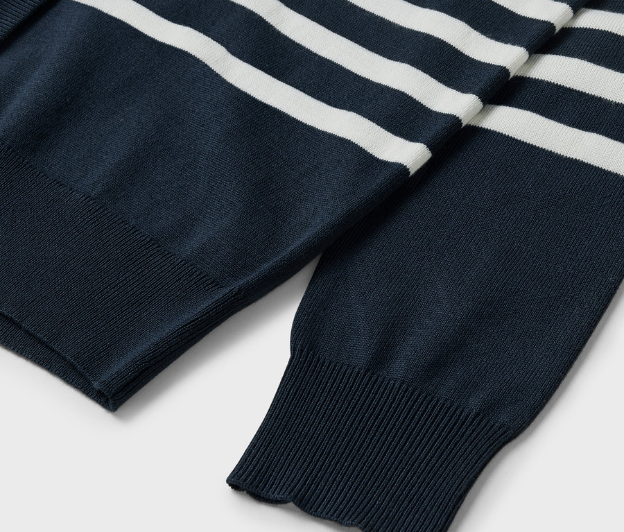 Detail modrého svetra s bielymi pruhmi, viditeľné rukávy a rebrovaný lem.