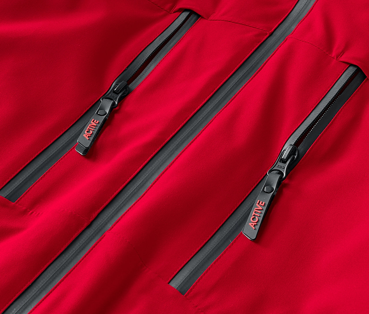 Detail červenej bundy s dvoma sivými zipsami, na ktorých je nápis ACTIVE.