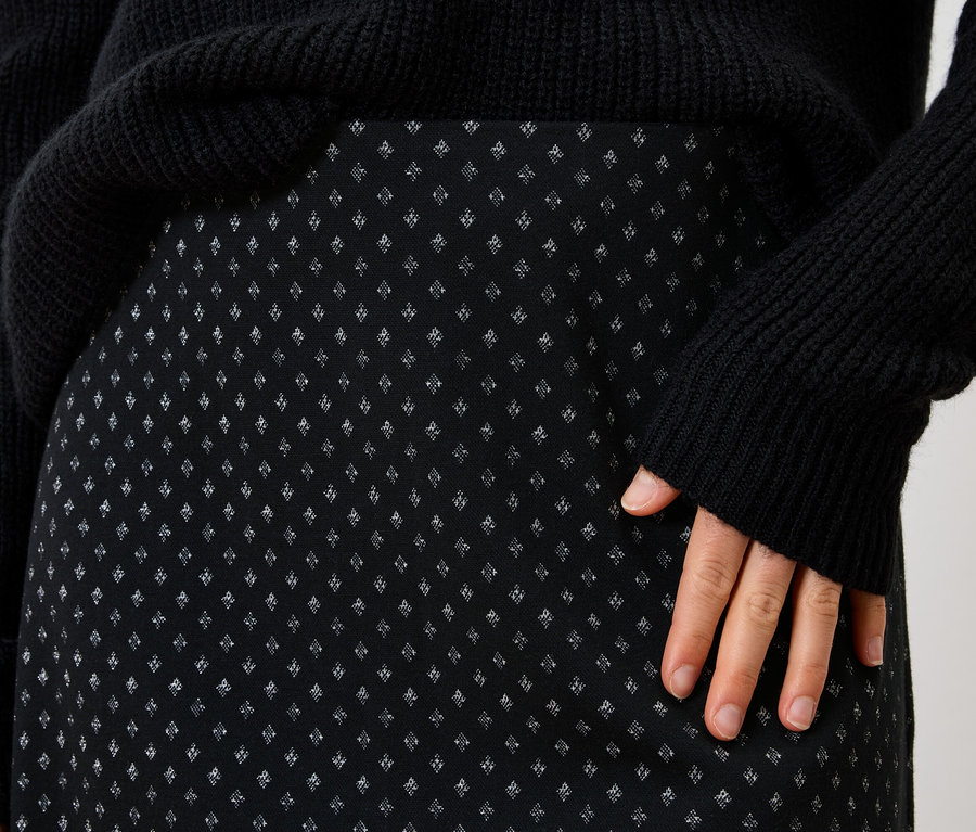 Detail čiernej dámskej sukne s drobným vzorom a čierneho svetra.