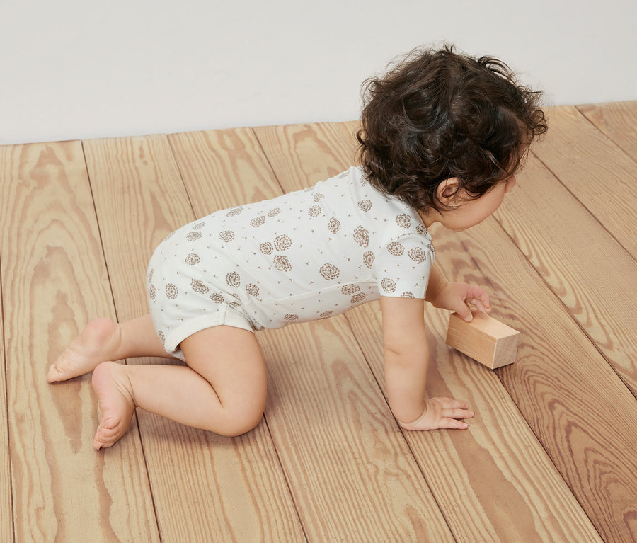 Batoľa lezie po drevenej podlahe v bielom body s krátkym rukávom, 5 ks, s možnosťou prispôsobenia veľkosti.