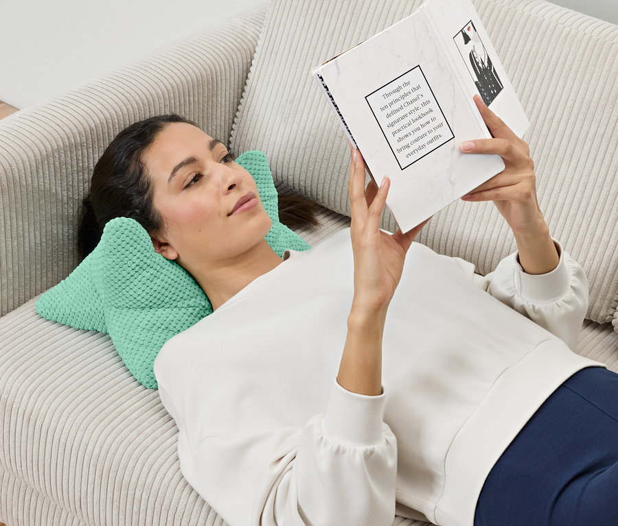 Žena leží na pohovke a číta si knihu, pričom jej hlava spočíva na vankúši na čítanie.