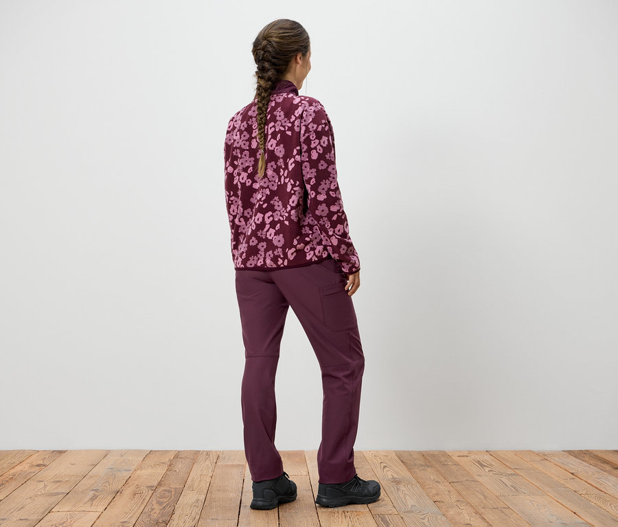 Žena so zapleteným vrkočom stojí chrbtom ku kamere a má na sebe fialovú mikinu s kvetinovým vzorom a fialové nohavice.